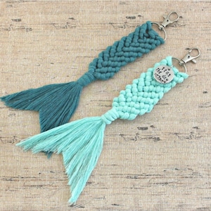 May include: Two teal and turquoise macrame mermaid tail keychains with silver key rings and a silver charm that says "Seas the day".