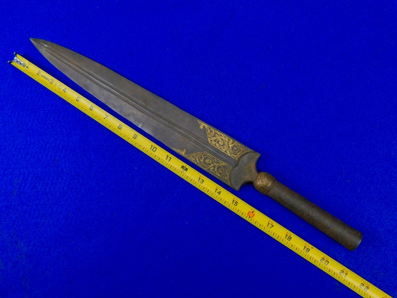 May include: A long, silver-colored dagger with a wooden handle and gold-colored decorative patterns. The dagger is measured against a yellow tape measure, showing it is approximately 19 inches long.