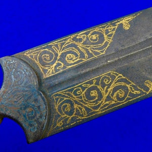 May include: Close-up of a sword blade with intricate gold floral designs etched into the metal. The blade is dark gray and the designs are a bright gold.