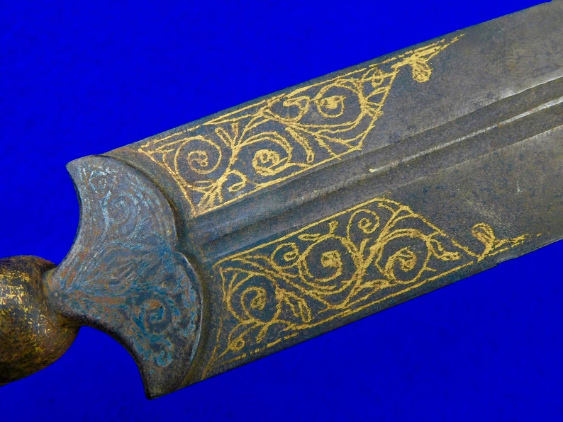 May include: Close-up of a sword blade with intricate gold floral designs etched into the metal. The blade is dark gray and the designs are a bright gold.