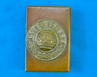 Puede incluir: Una caja rectangular de latón con un diseño circular que presenta una corona y el texto "Gott Mit Uns".