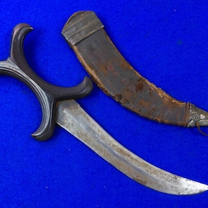 May include: A curved, silver-colored dagger with a black, intricately carved handle. The dagger is in a brown leather scabbard with silver accents.