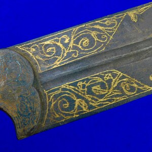 May include: Close-up of a sword blade with intricate gold-colored designs on a dark gray background.