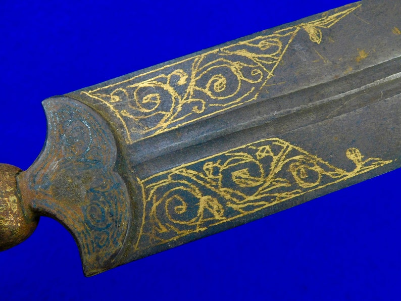 May include: Close-up of a sword blade with intricate gold-colored designs on a dark gray background.