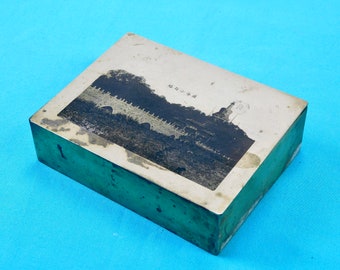 May include: A vintage silver metal box with a black and white photograph of a building with a pagoda on top. The text on the box reads "北 京 的 景", which translates to "Scenery of Beijing".