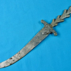 Könnte beinhalten: Ein silberfarbener Brieföffner mit einem dekorativen, verzierten Griff. Der Griff ist in Form eines stilisierten Blattes geformt und hat ein florales Design. Die Klinge ist gebogen und scharf.