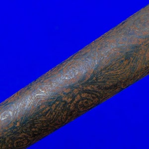 May include: Close-up of a long, dark brown metal rod with a swirling, textured pattern. The rod has a slightly rough surface and a dark, almost black, color.