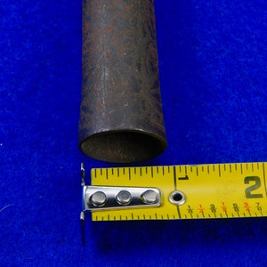 May include: Close-up of a rusty metal pipe with a diameter of 2 inches, measured with a yellow tape measure.