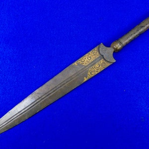May include: A long, silver-colored dagger with a gold-colored handle and intricate gold designs. The dagger has a sharp point and a double-edged blade.