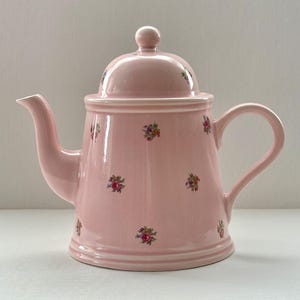 May include: A pink ceramic teapot with a floral pattern. The teapot has a lid and a handle.