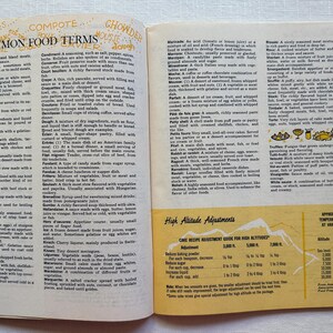 K&ouml;nnte beinhalten: Offenes Buch mit Seiten, die Vintage-Illustrationen und Text zeigen. Die linke Seite zeigt eine Liste von "Common Food Terms" mit Definitionen. Die rechte Seite enth&auml;lt eine Tabelle zu "High Altitude Adjustments" f&uuml;r das Backen.