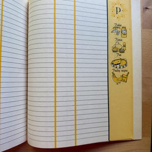 K&ouml;nnte beinhalten: Offenes Rezeptbuch mit linierten Seiten und gelben vertikalen Trennw&auml;nden. Die rechte Seite zeigt ein gelbes Feld mit dem Buchstaben "p" und Illustrationen von Essiggurken, Kuchen und anderen Lebensmitteln. Die W&ouml;rter "recipe", "book/page" und "comments" sind sichtbar.