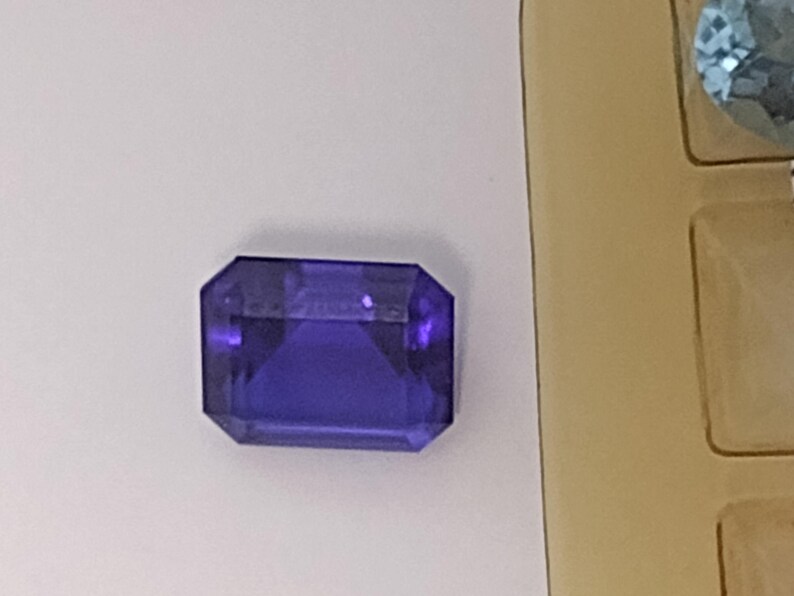 K&ouml;nnte beinhalten: Ein tiefvioletter Edelstein mit einem rechteckigen Smaragdschliff.