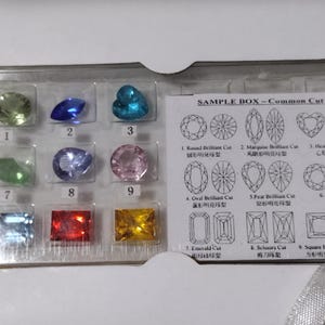 K&ouml;nnte beinhalten: Eine transparente Plastikbox mit verschiedenen Edelsteinproben. Die Box enth&auml;lt neun verschiedene Edelsteinschliffe, darunter Rundbrillant, Marquise, Herz, Oval, Birne, Mixed, Smaragd, Schere und quadratischer Brillant. Die Box enth&auml;lt auch ein Diagramm jedes Edelsteinschliffs.