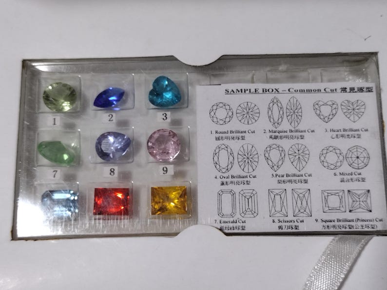 K&ouml;nnte beinhalten: Eine transparente Plastikbox mit verschiedenen Edelsteinproben. Die Box enth&auml;lt neun verschiedene Edelsteinschliffe, darunter Rundbrillant, Marquise, Herz, Oval, Birne, Mixed, Smaragd, Schere und quadratischer Brillant. Die Box enth&auml;lt auch ein Diagramm jedes Edelsteinschliffs.