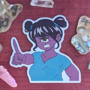 Puede incluir: Una pegatina con un personaje morado de estilo anime con un ojo, cabello oscuro en moños y una camisa azul con lunares. El personaje está señalando con un dedo y tiene una expresión de enojo. La pegatina está rodeada de conchas y cristales decorativos.