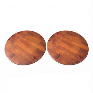 May include: Two circular tabletops made of medium-toned brown wood with a visible grain pattern. Each tabletop features a smooth, flat surface constructed from multiple joined wooden planks, displaying natural variations in color and texture.