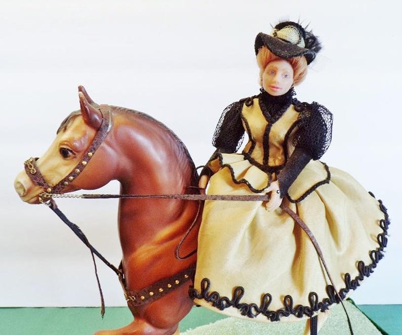 May include: A doll depicting a woman riding a brown horse. The woman is dressed in a yellow gown with black trim and a black hat. The horse has a detailed bridle and reins.