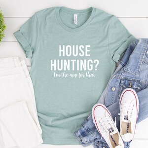 May include: A light blue t-shirt with the text "HOUSE HUNTING? I'm the app for that" in white.