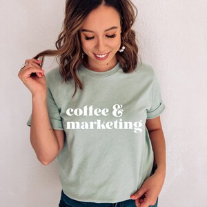 Op de afbeelding: Een lichtgroen t-shirt met de tekst "coffee & marketing" in wit retro-lettertype.