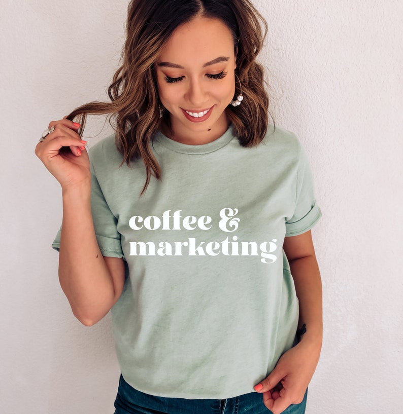 Op de afbeelding: Een lichtgroen t-shirt met de tekst "coffee & marketing" in wit retro-lettertype.