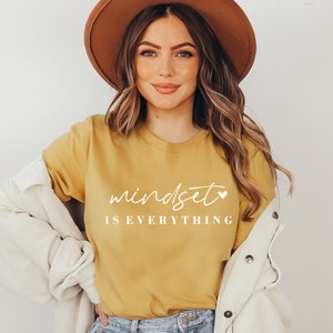 May include: A yellow t-shirt with the text "mindset is everything" in white with a small heart symbol after the word "mindset".