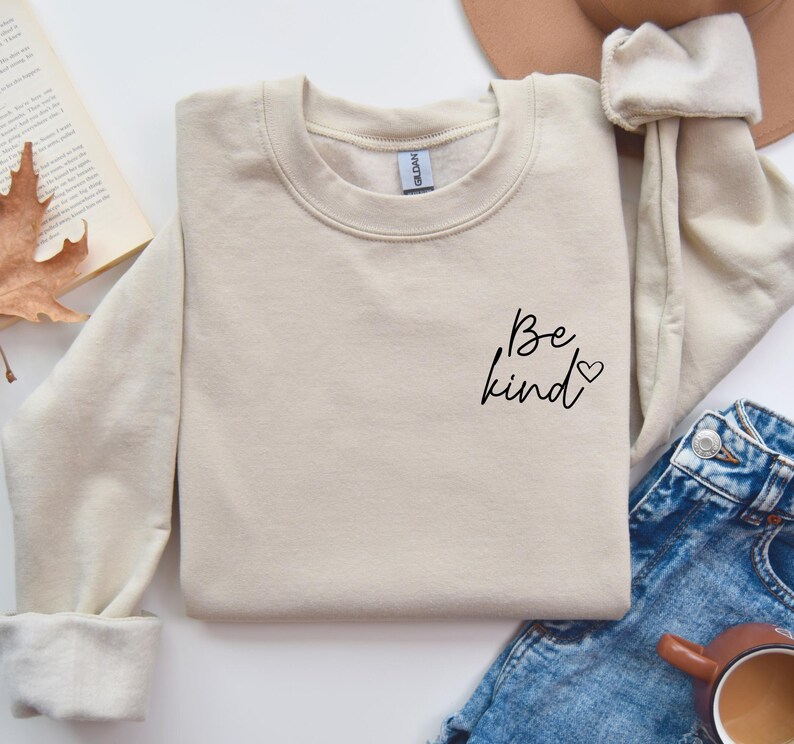 May include: A beige sweatshirt with the text "Be kind" and a small heart on the left side of the chest.