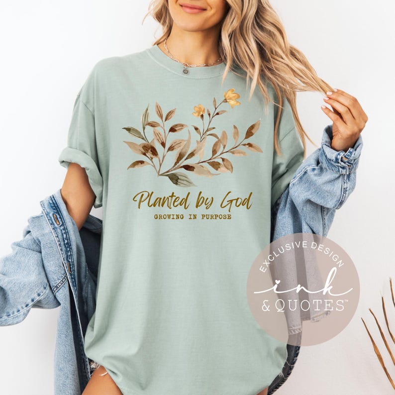 May include: A light green t-shirt with the text "Planted by God" and a floral design in brown and yellow. The shirt also has the text "Growing in Purpose". A circular logo with the text "Exclusive Design Ink & Quotes" is visible.
