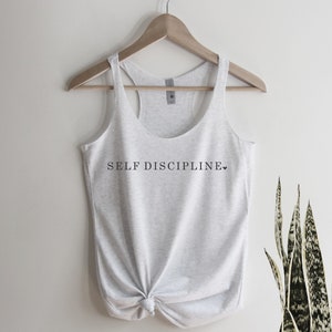 May include: A grey tank top with the text "SELF DISCIPLINE" printed on the front. The text is in black and there is a small heart symbol after the word "DISCIPLINE".