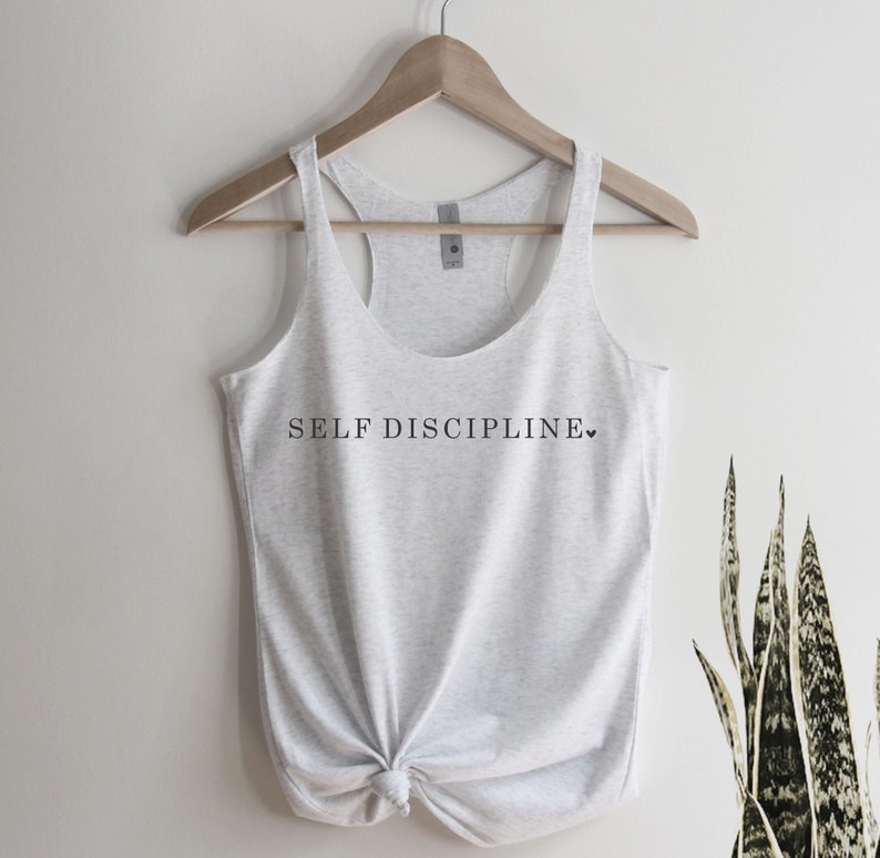 May include: A grey tank top with the text "SELF DISCIPLINE" printed on the front. The text is in black and there is a small heart symbol after the word "DISCIPLINE".