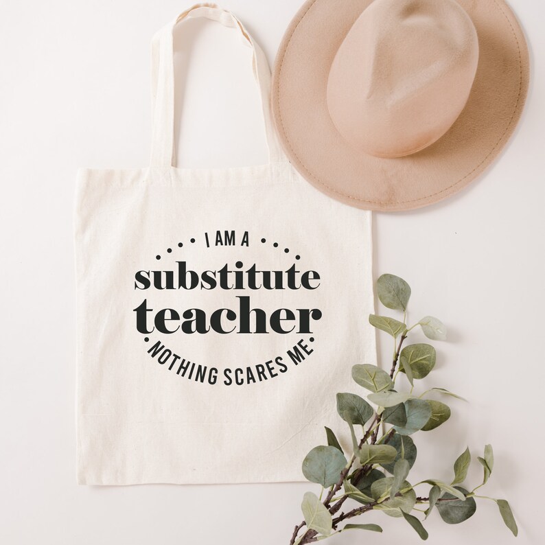Peut inclure: Un sac fourre-tout en toile blanche avec du texte noir qui dit "Je suis un professeur rempla&ccedil;ant. Rien ne me fait peur."