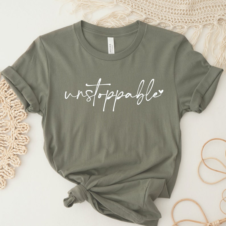 Op de afbeelding: Een groen T-shirt met het woord "unstoppable" in witte cursieve letters met een klein hartje.