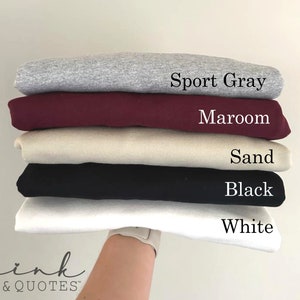 May include: Stack of five t-shirts in different colors: Sport Gray, Maroon, Sand, Black, and White.