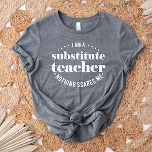 Peut inclure: T-shirt gris avec un texte blanc qui dit "Je suis un professeur rempla&ccedil;ant. Rien ne me fait peur."