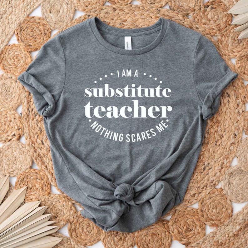Peut inclure: T-shirt gris avec un texte blanc qui dit "Je suis un professeur rempla&ccedil;ant. Rien ne me fait peur."