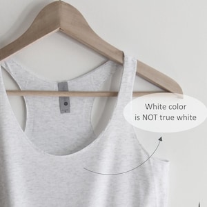 May include: A white tank top hanging on a wooden hanger. The white colour is not true white.