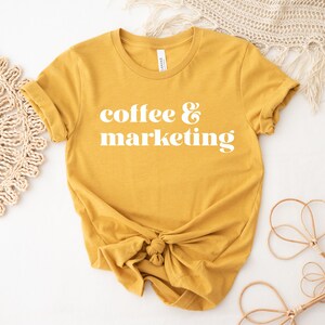 Op de afbeelding: Een mosterdgeel T-shirt met de tekst "coffee & marketing" in wit.