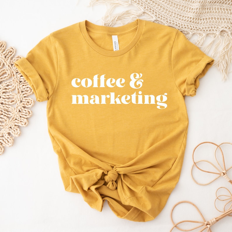 Op de afbeelding: Een mosterdgeel T-shirt met de tekst "coffee & marketing" in wit.