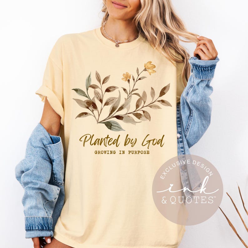 May include: Cream-colored t-shirt with the text "Planted by God" and a floral design in brown and yellow. The shirt also has the text "Growing in Purpose" below the main text.