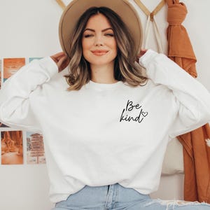 May include: White sweatshirt with a black cursive inscription that reads "Be kind" with a small heart symbol.