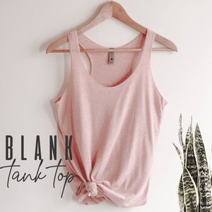May include: A light pink sleeveless tank top with a scoop neck, hanging on a wooden hanger. The tank top is made of a soft, textured fabric and has a knotted bottom.