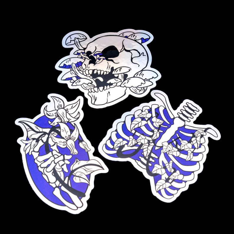 May include: Three sticker designs featuring a skull with mushrooms, a ribcage with vines, and a hand skeleton with flowers. The stickers are white with black outlines and a blue gradient background.