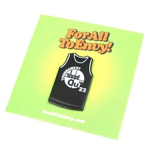 May include: Black and white enamel pin of a basketball jersey with the text "Tournament Shoot Out '23". The pin is on a green background with the text "For All To Envy!" in orange.