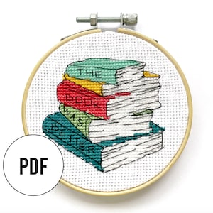 May include: A cross-stitch pattern of a stack of books with the text "The book was better" on the bottom book. The pattern is on a white background and is framed in a wooden hoop.