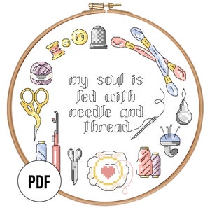 May include: A white embroidery hoop with a brown wooden frame. The hoop contains a cross-stitch design of various sewing tools and the text "my soul is fed with needle and thread".