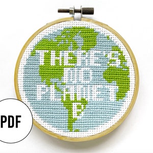 Puede incluir: Un aro de bordado de punto de cruz con una imagen bordada de la Tierra en verde y azul. El texto "There is only one Earth" está bordado en blanco sobre la imagen.