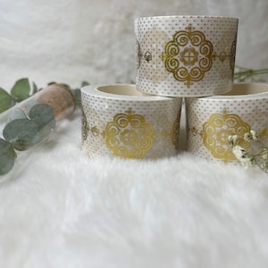 May include: Three rolls of white washi tape with gold patterned designs. The tape has a white background with gold polka dots and a gold floral pattern.