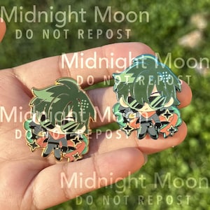 May include: Two enamel pins featuring a character with green hair, sunglasses, and a black outfit. The pins have gold-colored borders and star accents. The text "Midnight Moon DO NOT REPOST" is visible in the background.