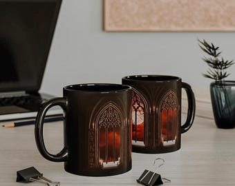 May include: Two black ceramic mugs featuring a gothic window design. The mugs are filled with a red and orange liquid. The mugs are on a wooden table.
