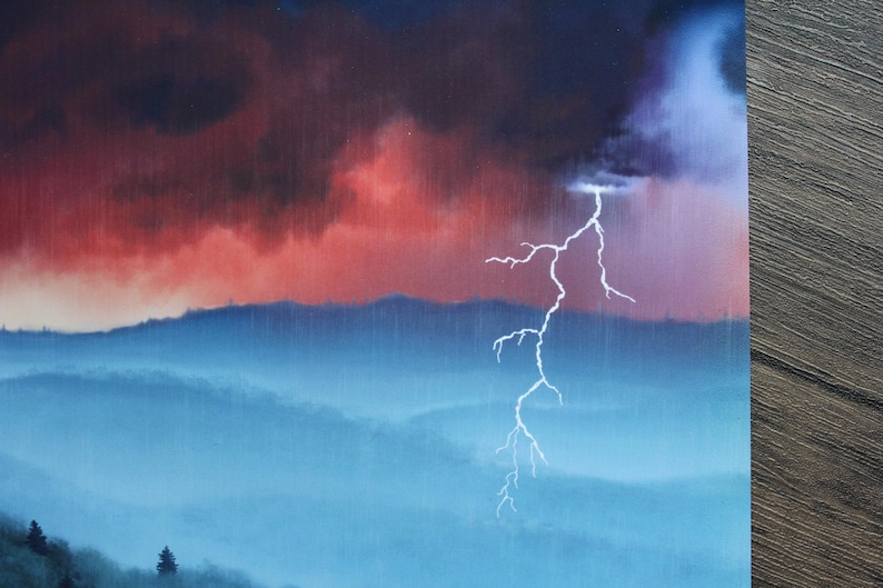以下が含まれることがあります： 山脈上空の劇的な雷雨の絵。空は濃い赤と紫の雲で満たされ、明るい白い稲妻が落ちています。雨は青い山々と木々に降っています。